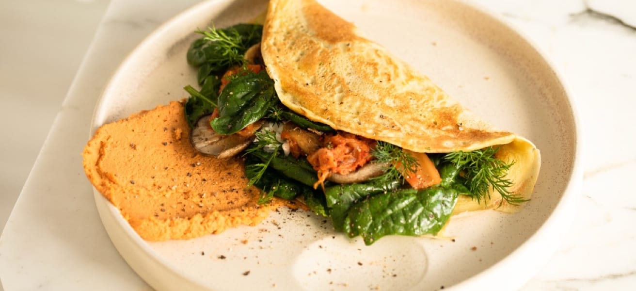 A folded omelette with spinach on a cream colored plate.